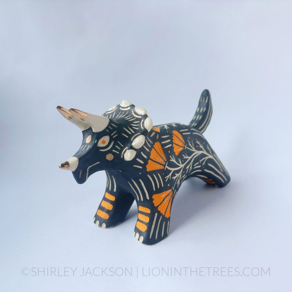 Black sgraffito Triceratops totem done with various underglaze, clear glaze, and gold luster.
