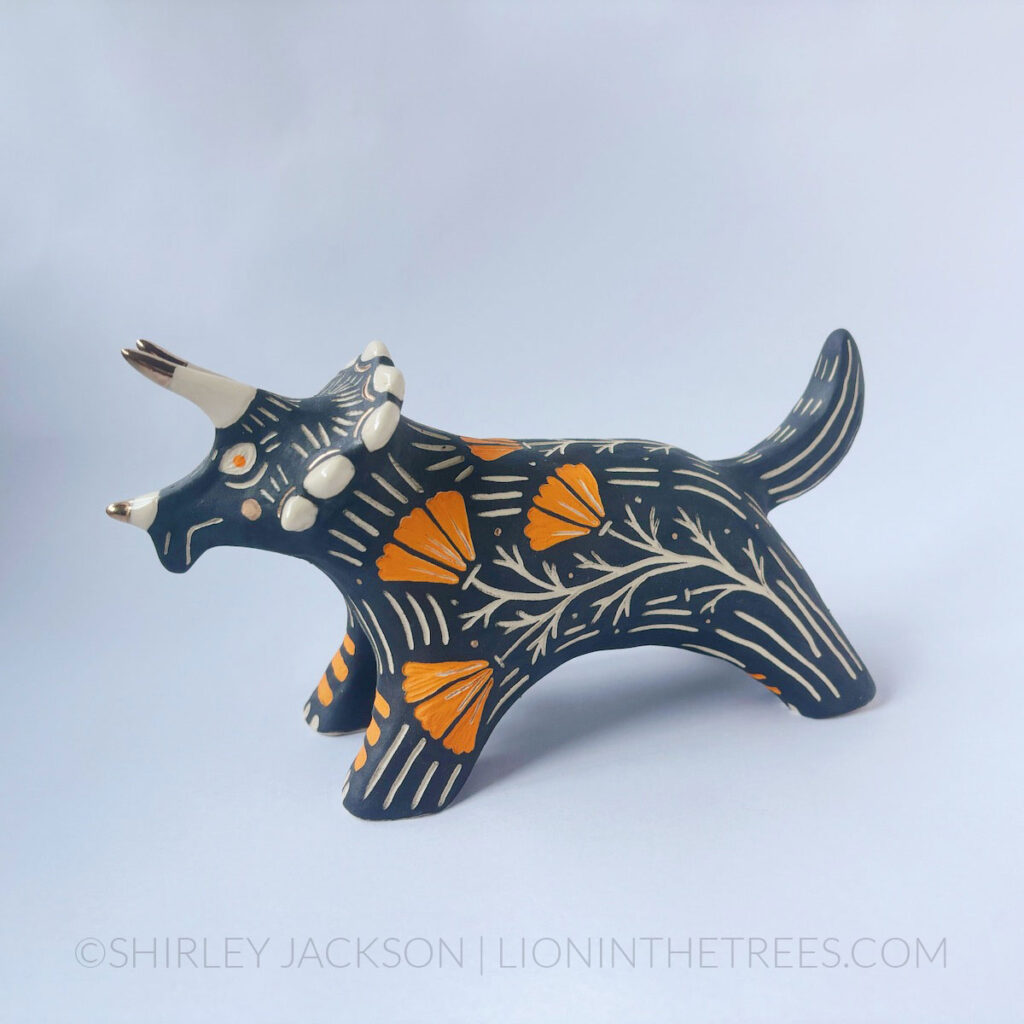 Black sgraffito Triceratops totem done with various underglaze, clear glaze, and gold luster.