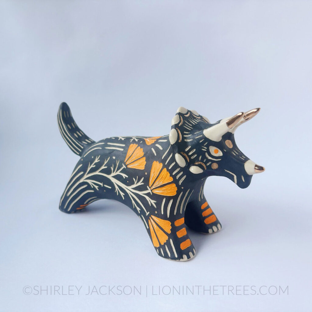 Black sgraffito Triceratops totem done with various underglaze, clear glaze, and gold luster.