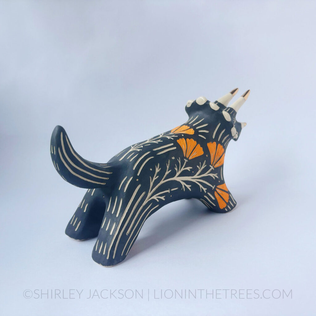 Black sgraffito Triceratops totem done with various underglaze, clear glaze, and gold luster.