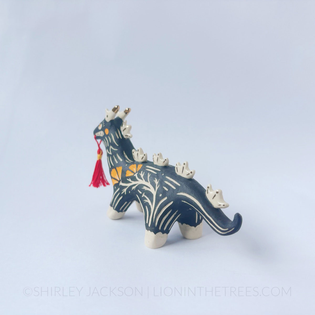 Sgraffito black dragon totem with a handmade red tassel hanging from it's mouth.