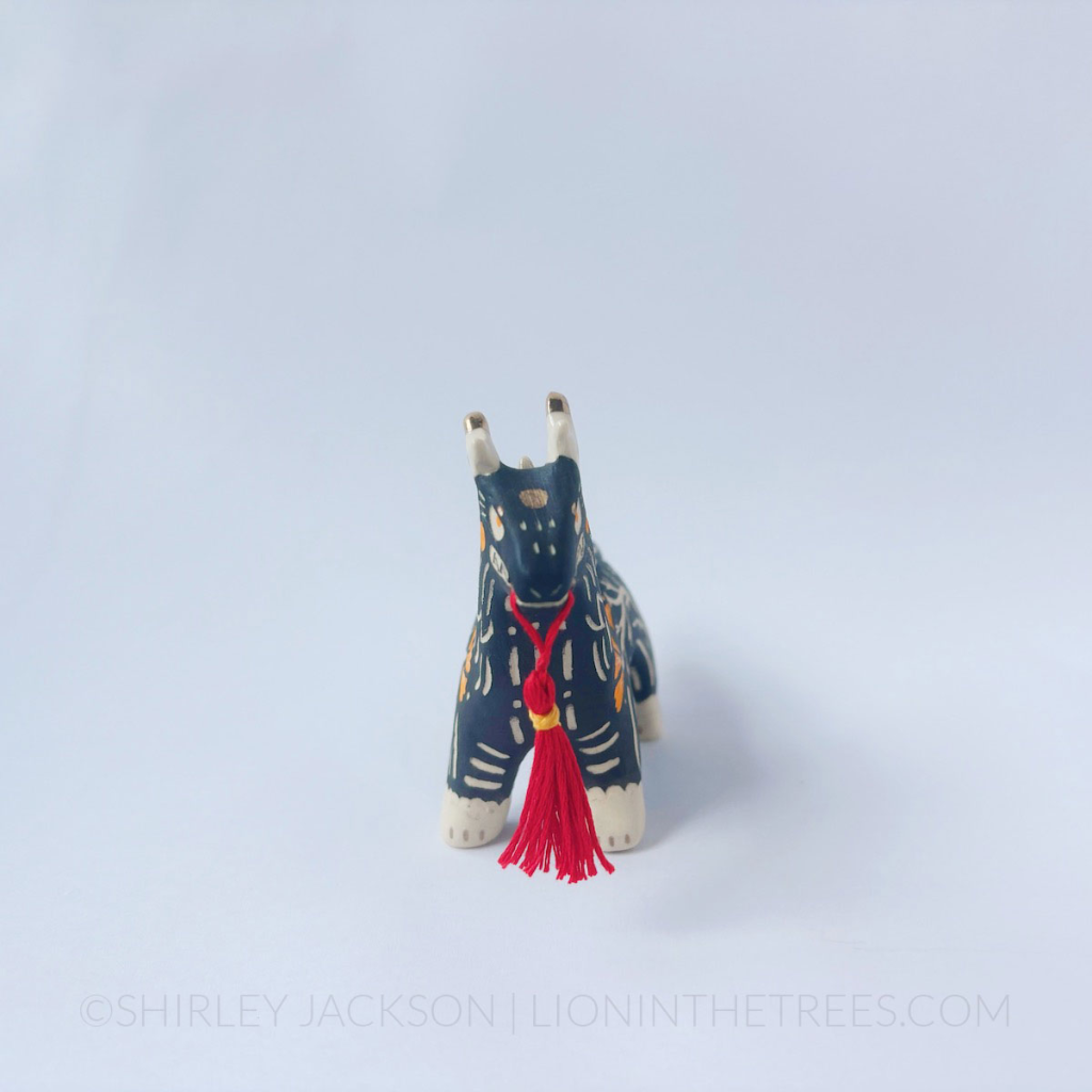 Sgraffito black dragon totem with a handmade red tassel hanging from it's mouth.