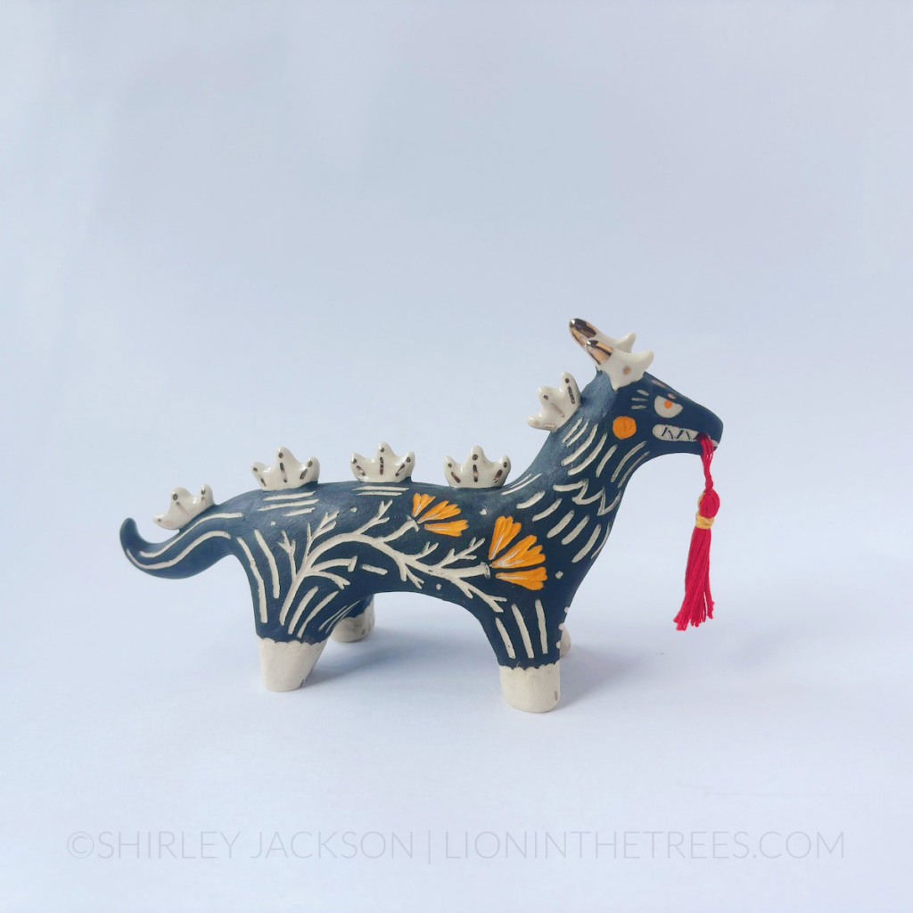 Sgraffito black dragon totem with a handmade red tassel hanging from it's mouth.