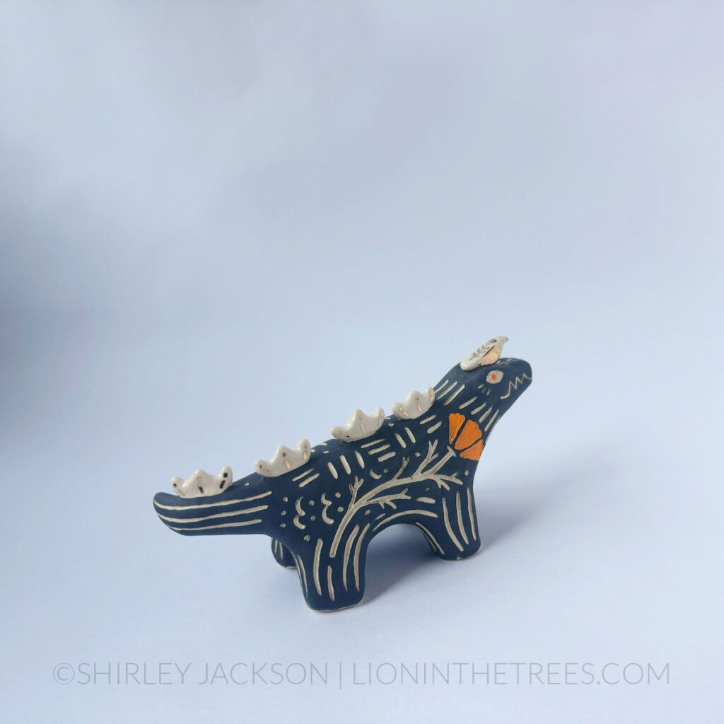 Black sgraffito alligator with a little friend totem done with various underglazes, clear glaze, and gold luster.