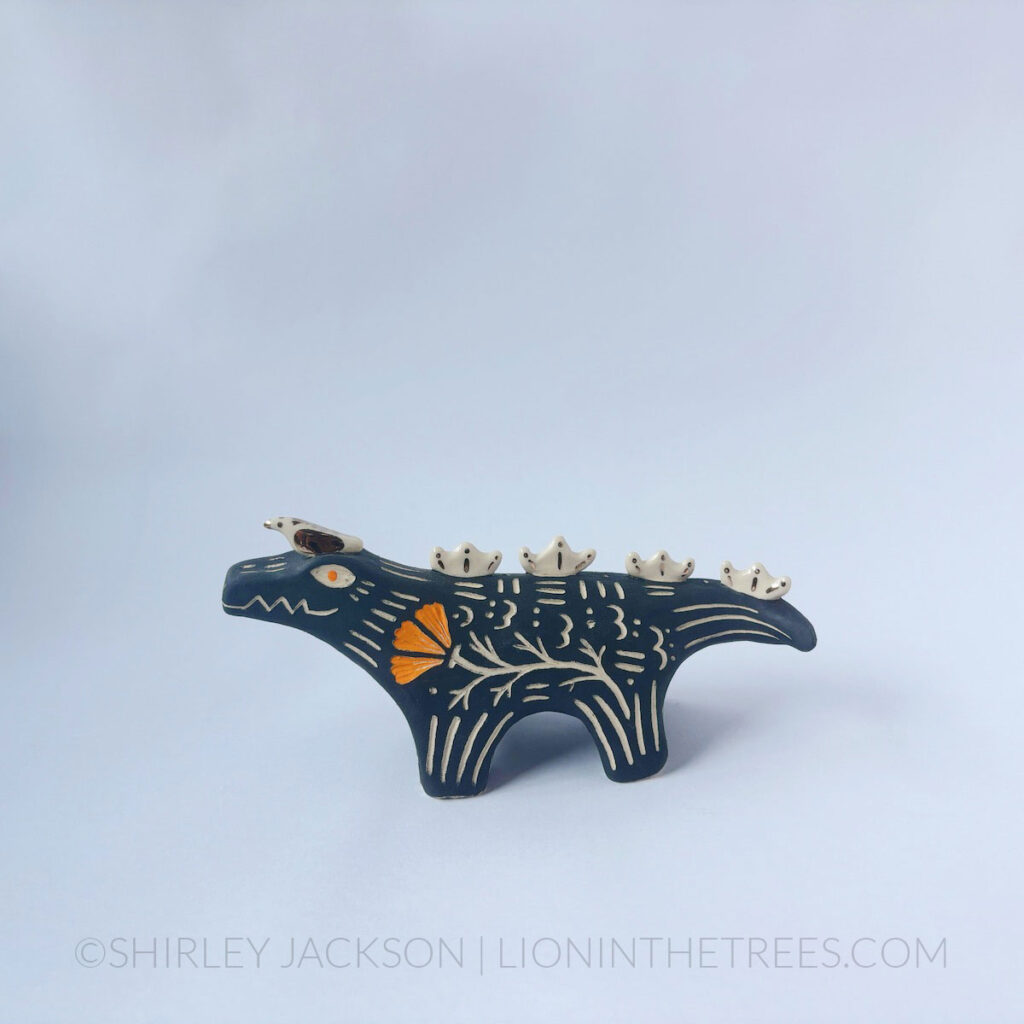 Black sgraffito alligator with a little friend totem done with various underglazes, clear glaze, and gold luster.