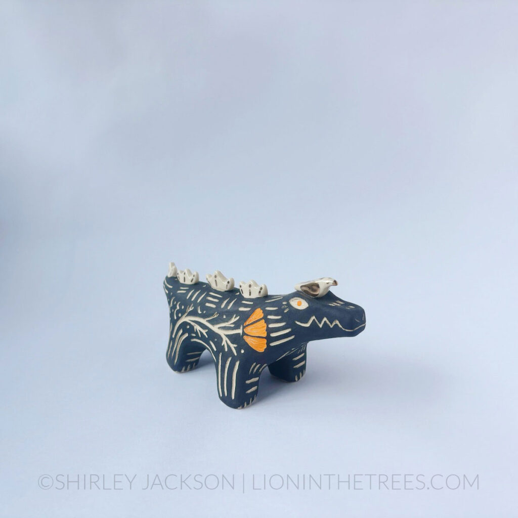 Black sgraffito alligator with a little friend totem done with various underglazes, clear glaze, and gold luster.