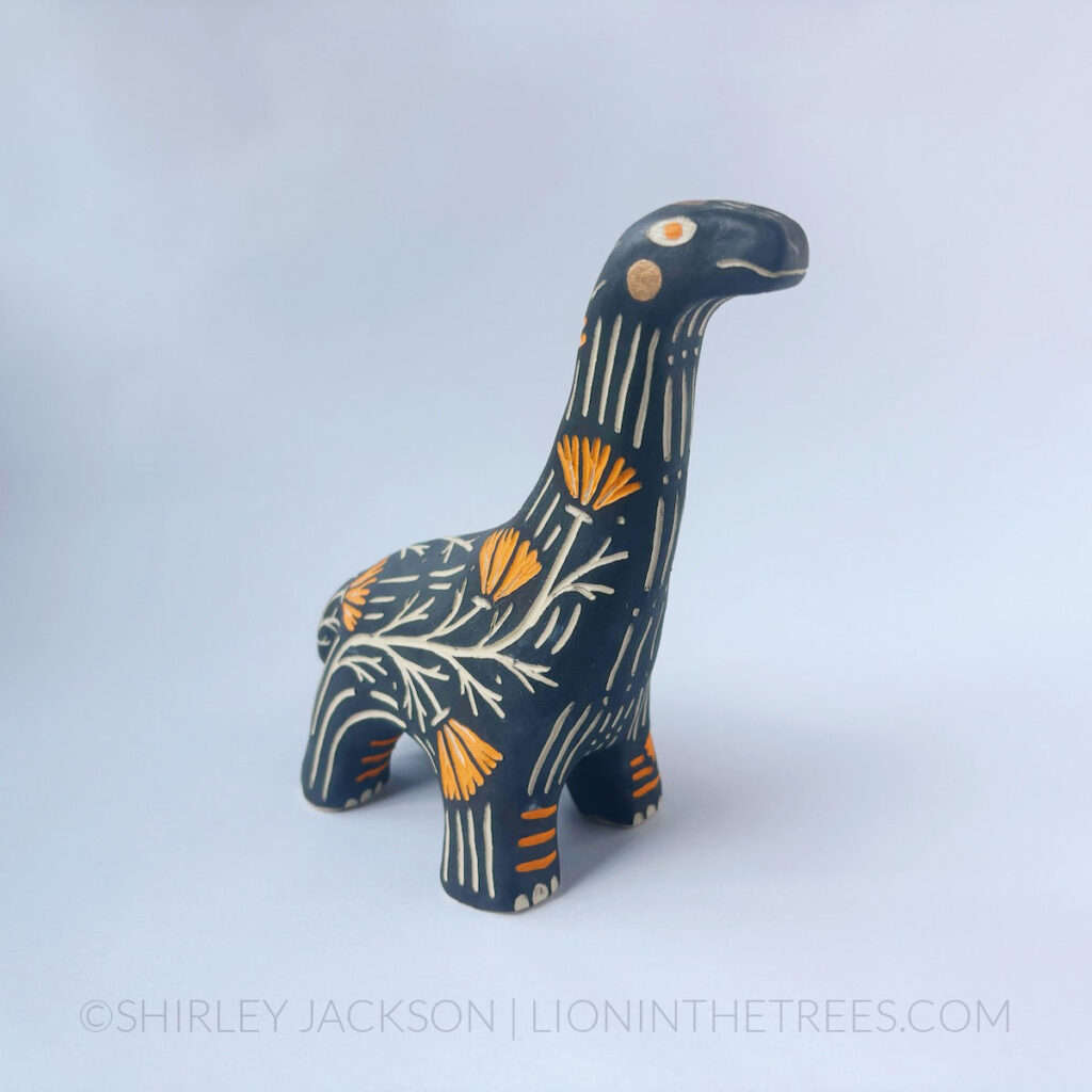 Black sgraffito Brontosaurus totem done with various underglazes and gold gilding.