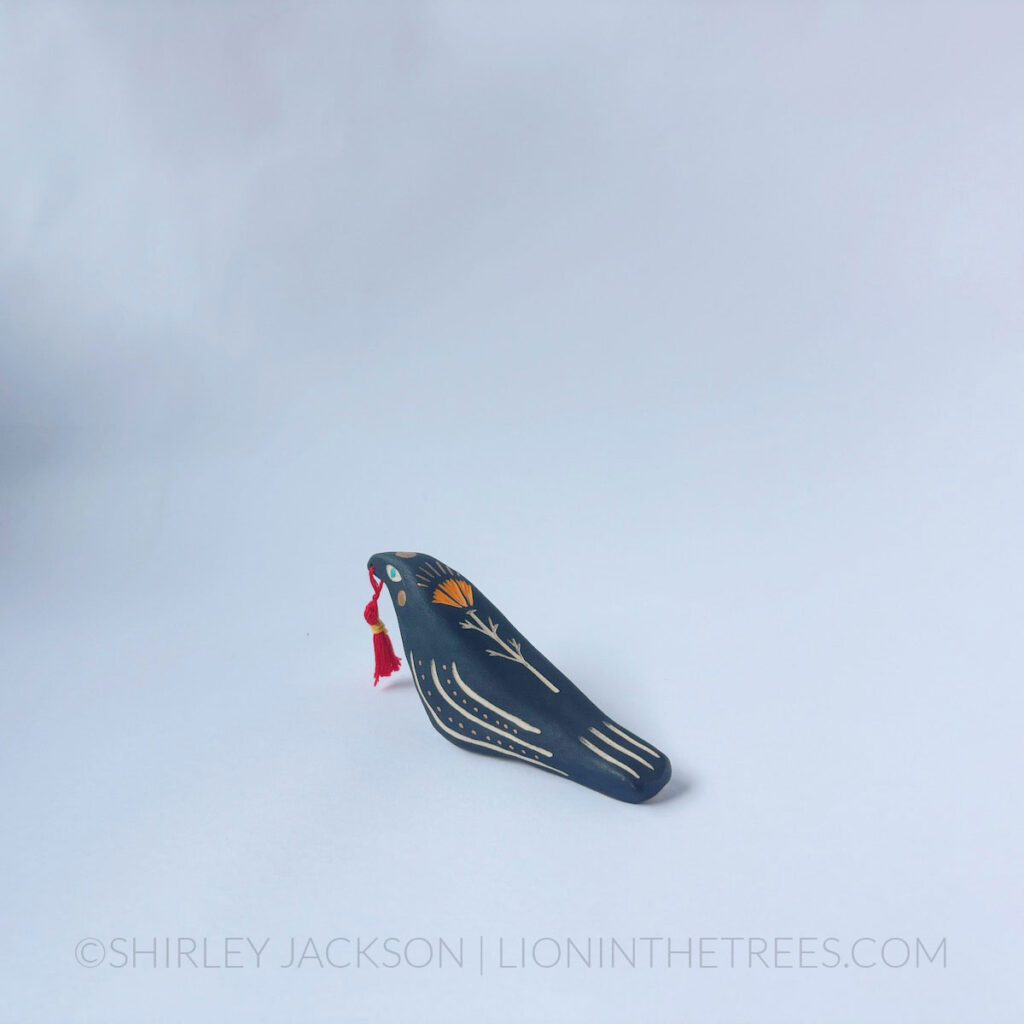 Raven totem done with various underglaze, gold gilding, and a handmade tassel.