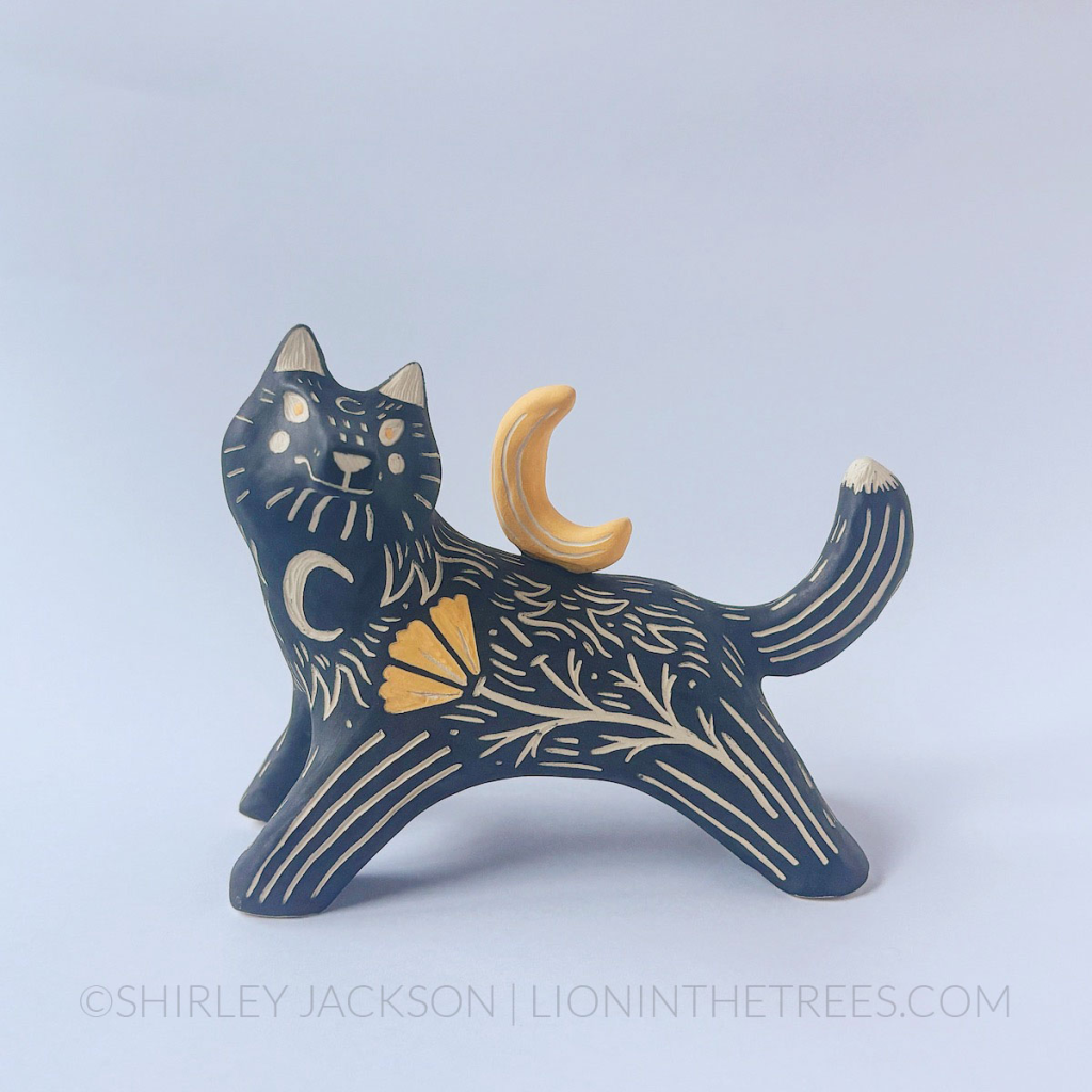 A front view of a ceramic black underglaze wolf sculpture posed as though it's leaping or running. It has it's head arched back and a crescent moon sculpture on it's back. There are sgraffito markings all along it's body including a crescent moon on the chest and a California Poppy done with a yellow underglaze.