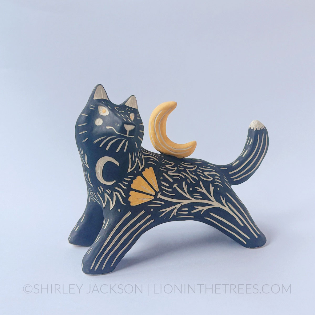 A front view of a ceramic black underglaze wolf sculpture posed as though it's leaping or running. It has it's head arched back and a crescent moon sculpture on it's back. There are sgraffito markings all along it's body including a crescent moon on the chest and a California Poppy done with a yellow underglaze.