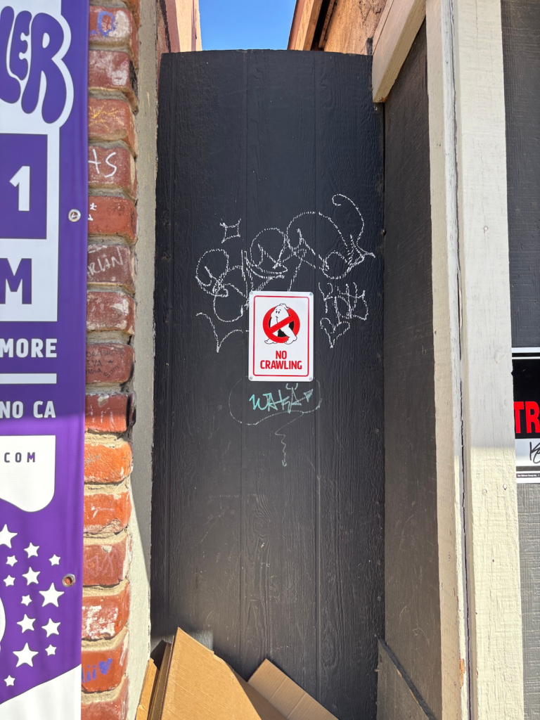A sign pinned up in an alleyway that says "NO CRAWLING" and has a ghostbusters-like logo but a Fresno Nightcrawler instead of a ghost.