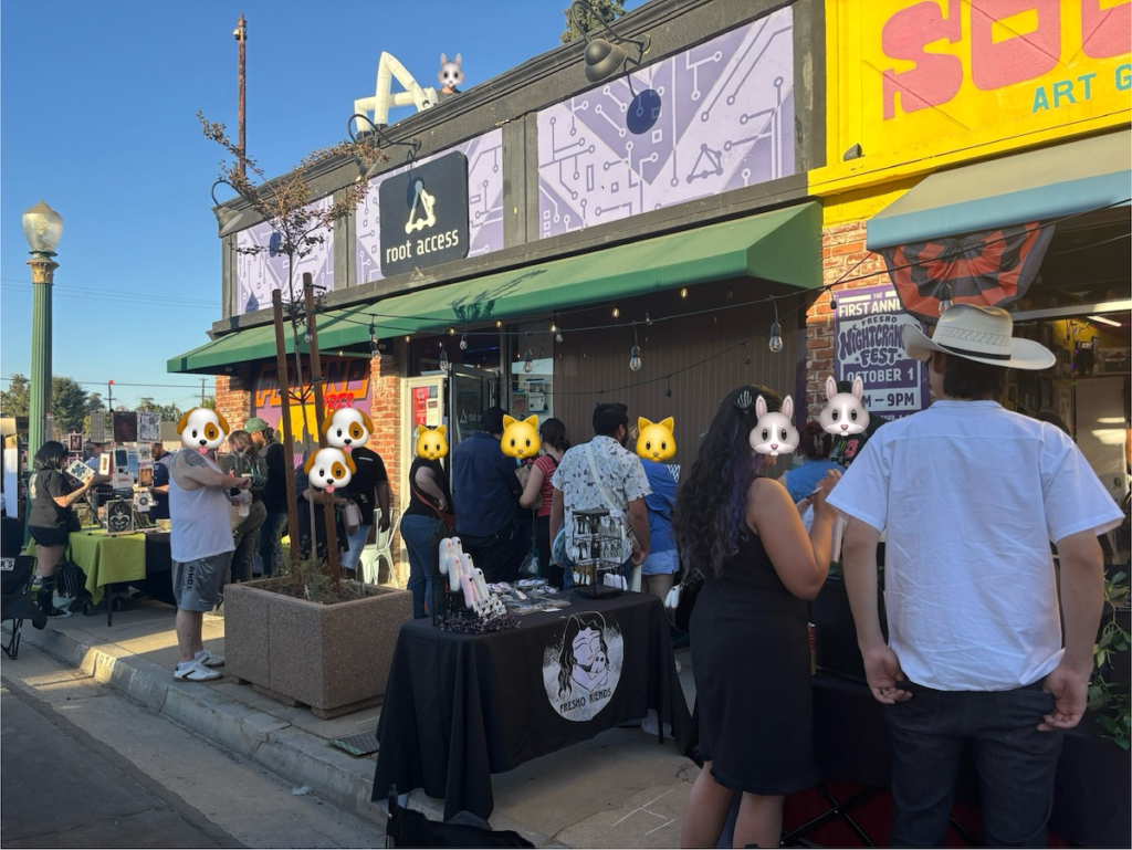 A photo showing people beginning to gather around vendor tables on the sidewalk outside of Sour Milk and Root Access. Cute animal emoji stickers have been applied to visible faces to protect privacy.