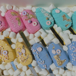 A group of delicious looking baked goods decorated with pastel pinks, turquoise, yellow, and blue.